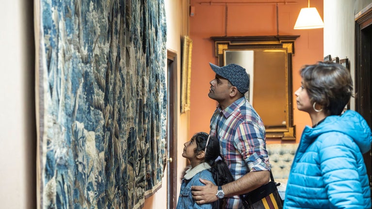 Visitors in the house at Sizergh. A young girl and her parents looking up at an intricate tapestry on the wall.